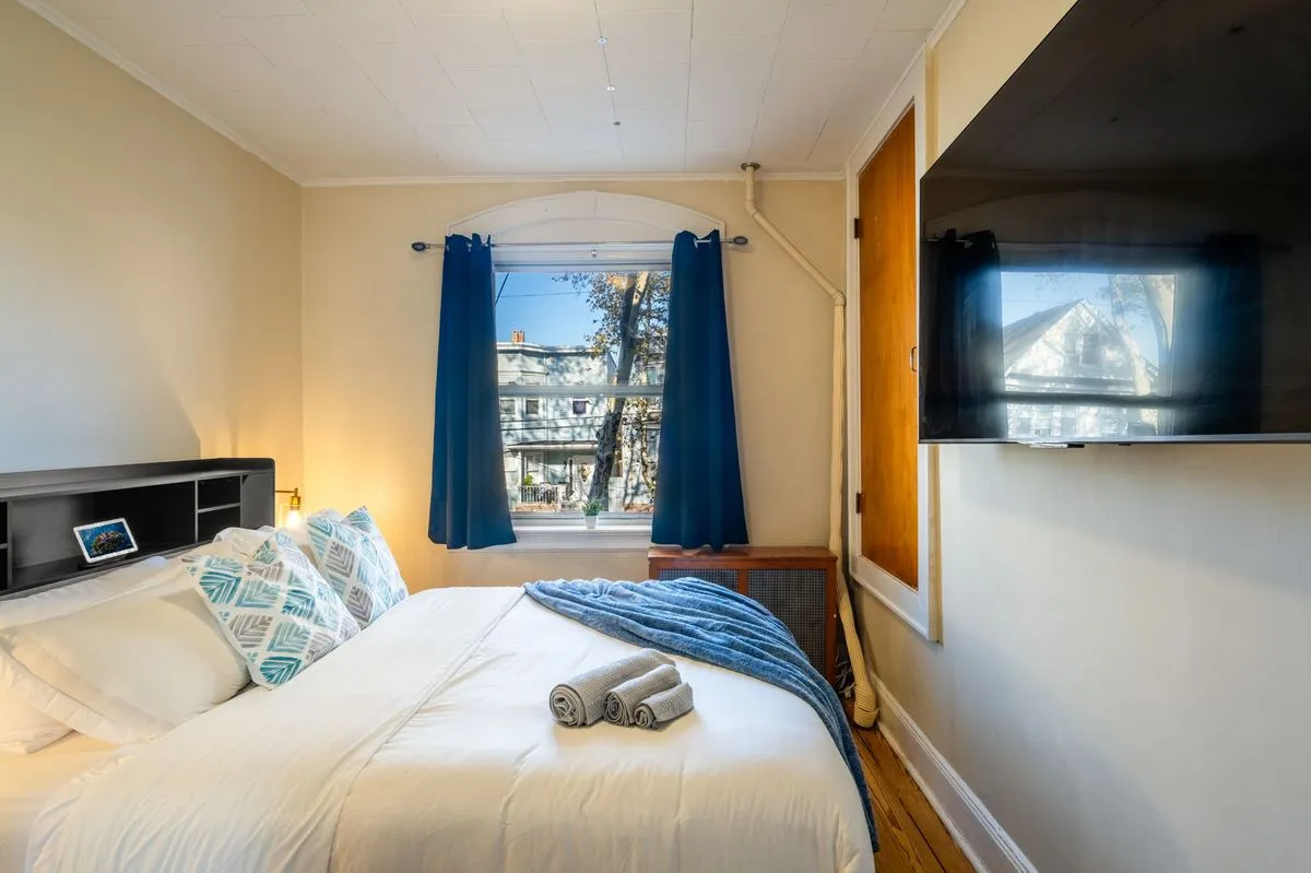 Queen bed with white linens, blue curtains, and a wall-mounted smart TV