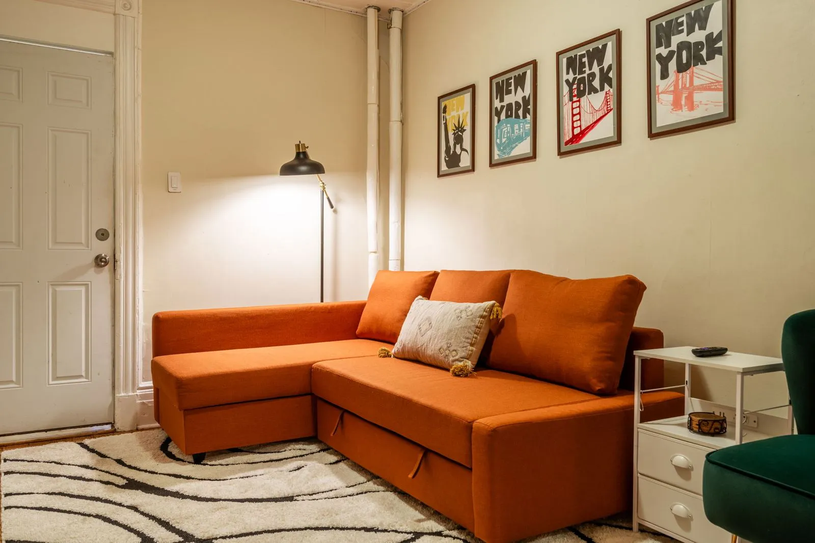 Living room with a burnt orange sectional sofa, floor lamp, and hand-painted New York posters