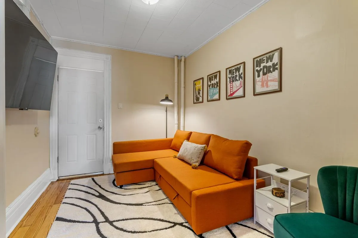 Living room with orange sectional, smart TV, and New York art prints
